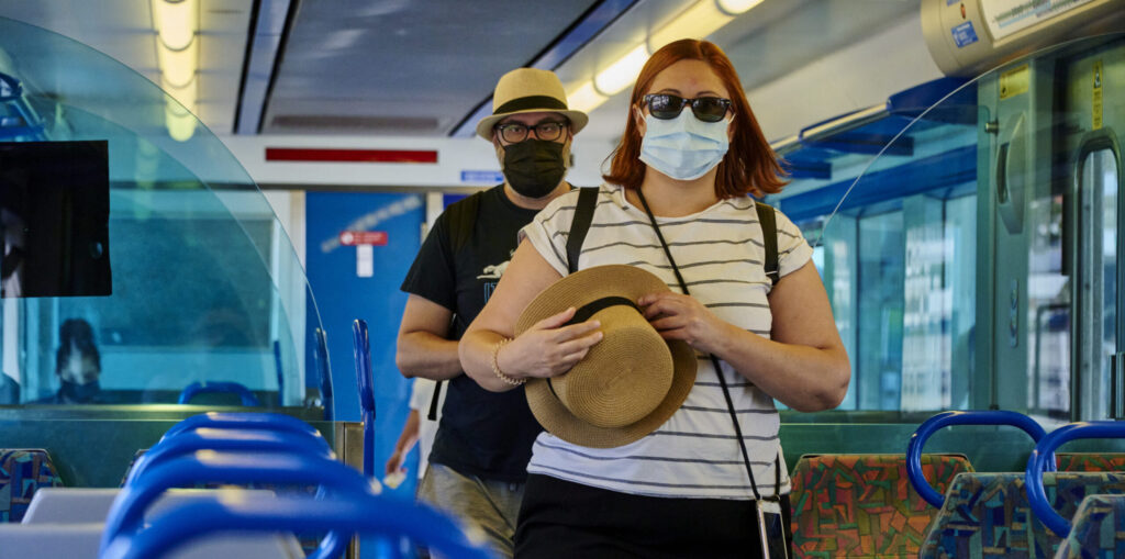 Woman in sunglasses, man in mask. All on bus.